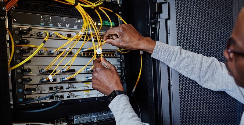 Close up of IT engineer connecting cables in server room while setting up data network, copy space